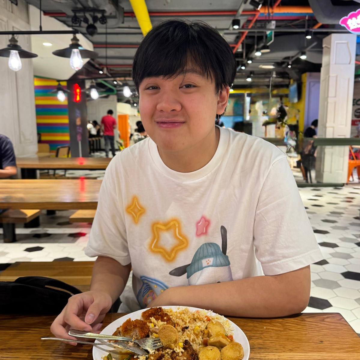 Lucius at a food court, grinning behind a plate of cutlet rice and tofu